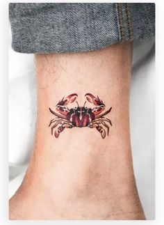 a small crab tattoo on the ankle with red watercolors and black dots around it