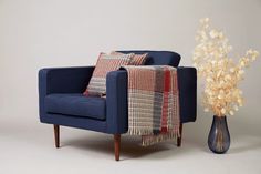 a blue chair next to a vase with flowers in it and a plaid throw pillow