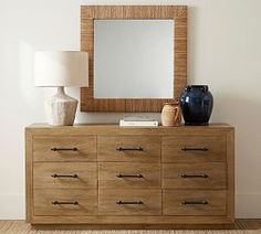 a wooden dresser with a mirror and vase on it in front of a white wall