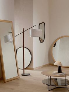 a living room filled with furniture next to a mirror and floor lamp on top of a hard wood floor