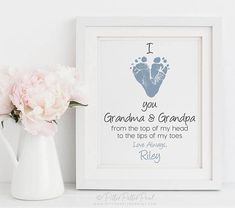 a white vase filled with pink flowers next to a framed baby's foot print