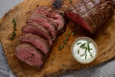 steak sliced up on a cutting board next to a small bowl of sour cream and fresh herbs