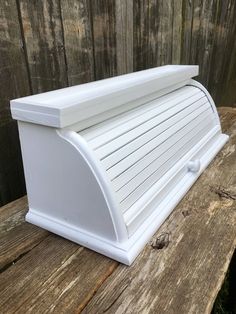 a white plastic mailbox sitting on top of a wooden bench next to a fence