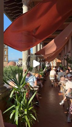 people sitting at tables under an awning on a patio with red cloths hanging from the ceiling