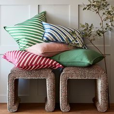 a pile of pillows sitting on top of two stools in front of a wall