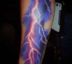 a man's arm with a lightning tattoo on it and a cell phone in the background