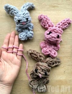 three small crocheted bunnies being held by someone's hand on a wooden surface