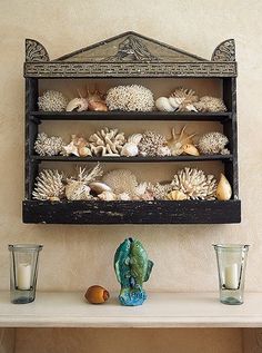 a shelf filled with seashells and candles on top of a table next to two glasses