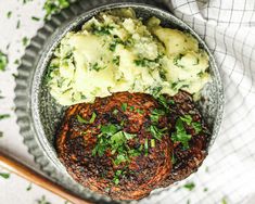 a bowl filled with mashed potatoes, meat and green garnish on top of a white table cloth