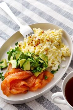 eggs, salmon and avocado on a white plate with a cup of tea