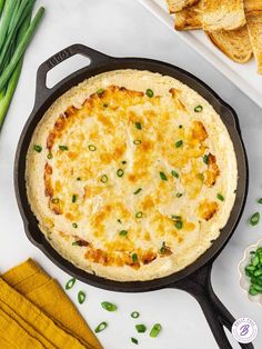 a skillet filled with cheesy potatoes and green onions on a white surface