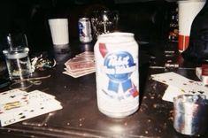 a can of beer sitting on top of a table next to glasses and other items