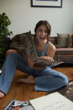 a woman is sitting on the floor and smiling while holding a book in her hands