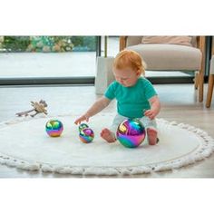 a baby playing with three shiny balls on the floor