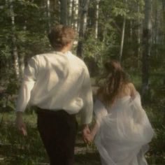 a man and woman walking through the woods holding hands