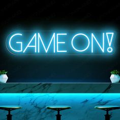 a neon sign that says game on above three stools in front of a marble counter