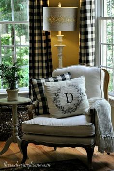 a chair with pillows on it in front of a window and a table with a lamp