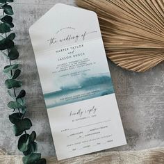 the wedding stationery is set on top of a table with greenery and a fan