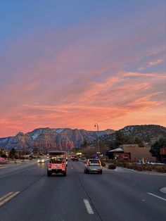 cars driving down the road at dusk with mountains in the background