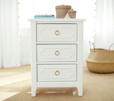 a white chest of drawers sitting on top of a carpeted floor next to a basket