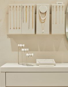 a white table topped with lots of necklaces next to a wall mounted jewelry rack