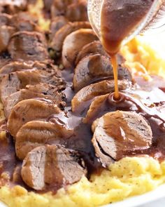 someone drizzling sauce over some meat on top of mashed potatoes with gravy