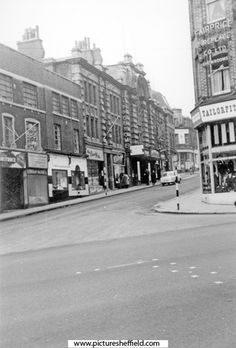 an old black and white photo of a street corner with buildings on both sides in the distance