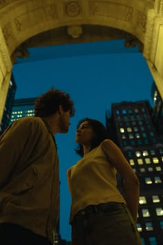 a man and woman standing in an archway looking at each other with buildings in the background