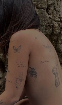 a woman with tattoos on her back sitting next to a stone wall