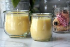 two candles sitting next to each other on top of a white marble counter with potted plants in the background