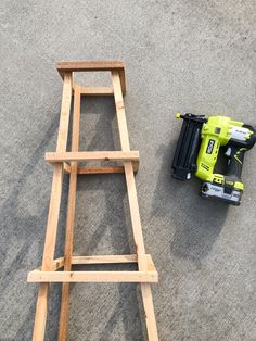 a wooden step ladder next to a cordless driller on the ground with a tool holder nearby