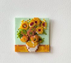 a cross - stitch flower arrangement on a white wall hanging from a hook with beads