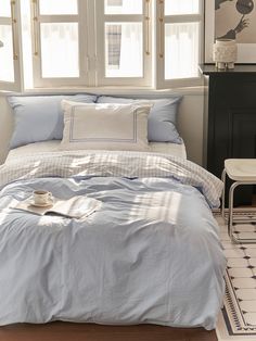 a bed with blue sheets and pillows in a room next to two windows that have white trim on them