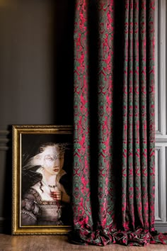 a painting on the floor next to a window with red and green curtains in front of it