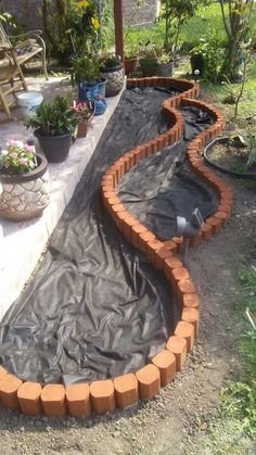 an outdoor garden area that is being constructed with bricks and plastic covering the ground, surrounded by potted plants