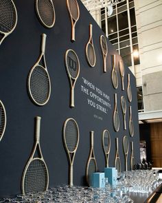 there are many tennis rackets hanging on the wall behind glasses and wine glasses in front of them