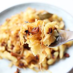 a spoon full of food on top of a white plate with bacon and pasta in it