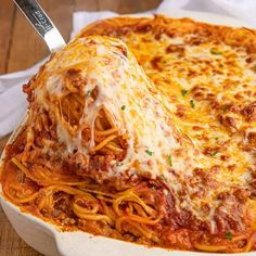 a large white casserole dish filled with spaghetti and sauce, on top of a wooden table