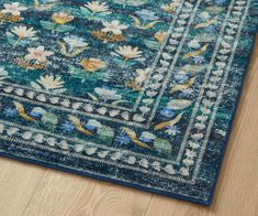 a blue area rug with flowers and leaves on the bottom, in front of a wooden floor