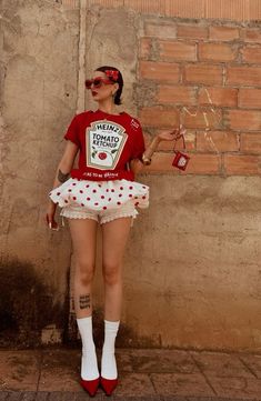 a woman in red shirt and polka dot skirt standing next to brick wall with sunglasses on