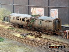 an old train car sitting on the tracks in front of a brick building with weeds growing out of it