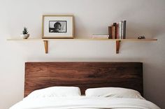 a bed with white linens and two wooden shelves on the wall above it,