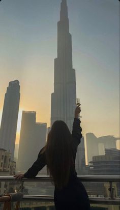 a woman standing on top of a tall building holding a wine glass in her hand