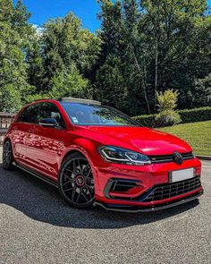 a red volkswagen car parked in front of some trees