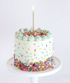 a white cake with sprinkles and a single candle on top is sitting on a plate