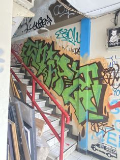 graffiti on the wall next to stairs in a building with white tile flooring and red handrails