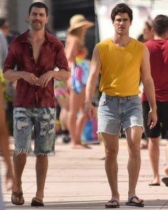 two men are walking down the street with other people in the background and one is wearing a yellow shirt