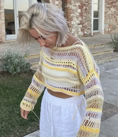 a woman with blonde hair wearing white pants and a yellow knitted cropped sweater