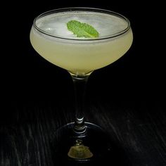 a drink with a green leaf on the rim in a glass sitting on a table