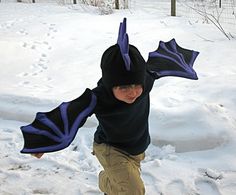 a young boy wearing a dragon costume riding a snowboard